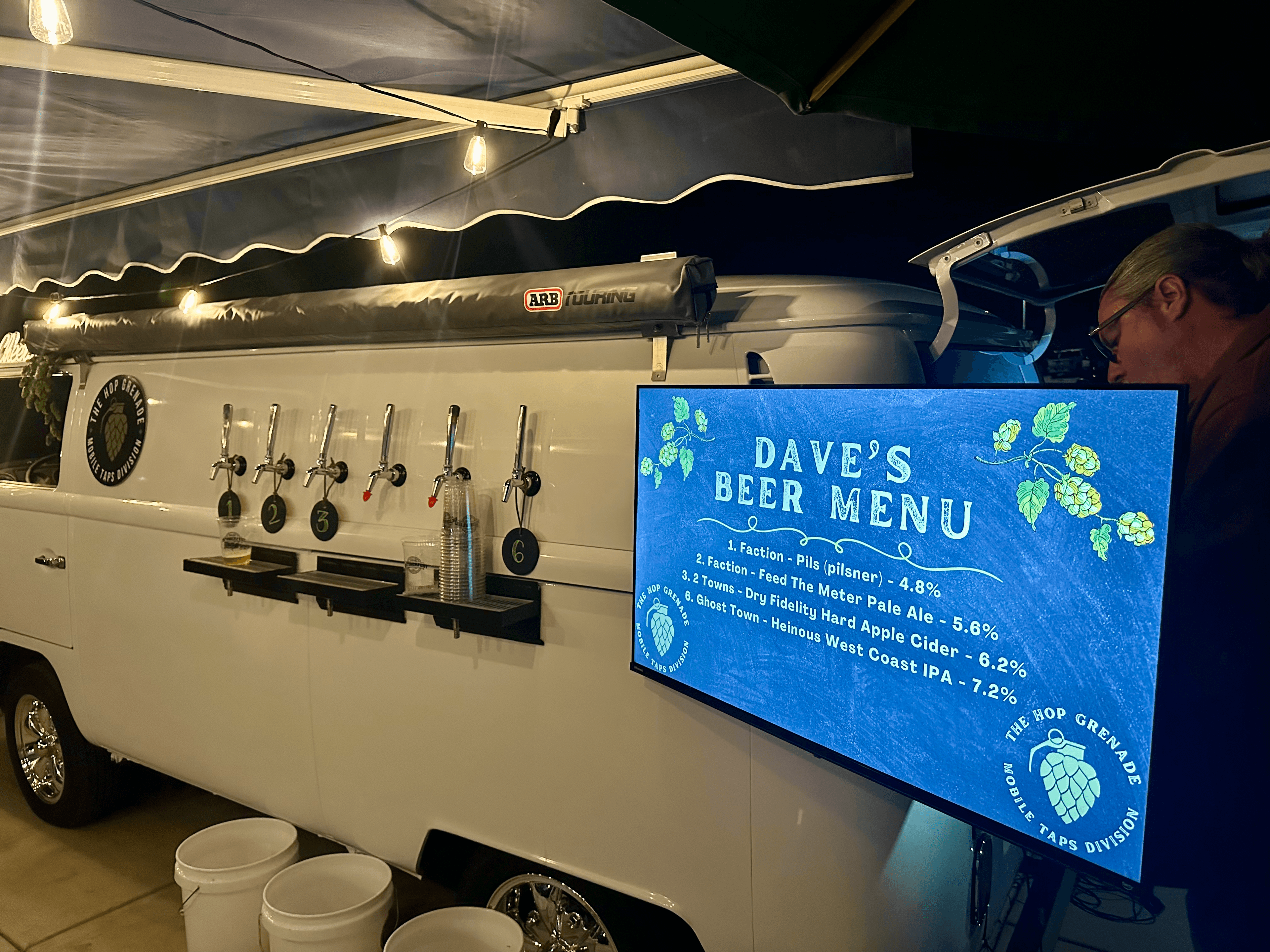 White mobile beer tap van with six taps and a digital menu screen at night.