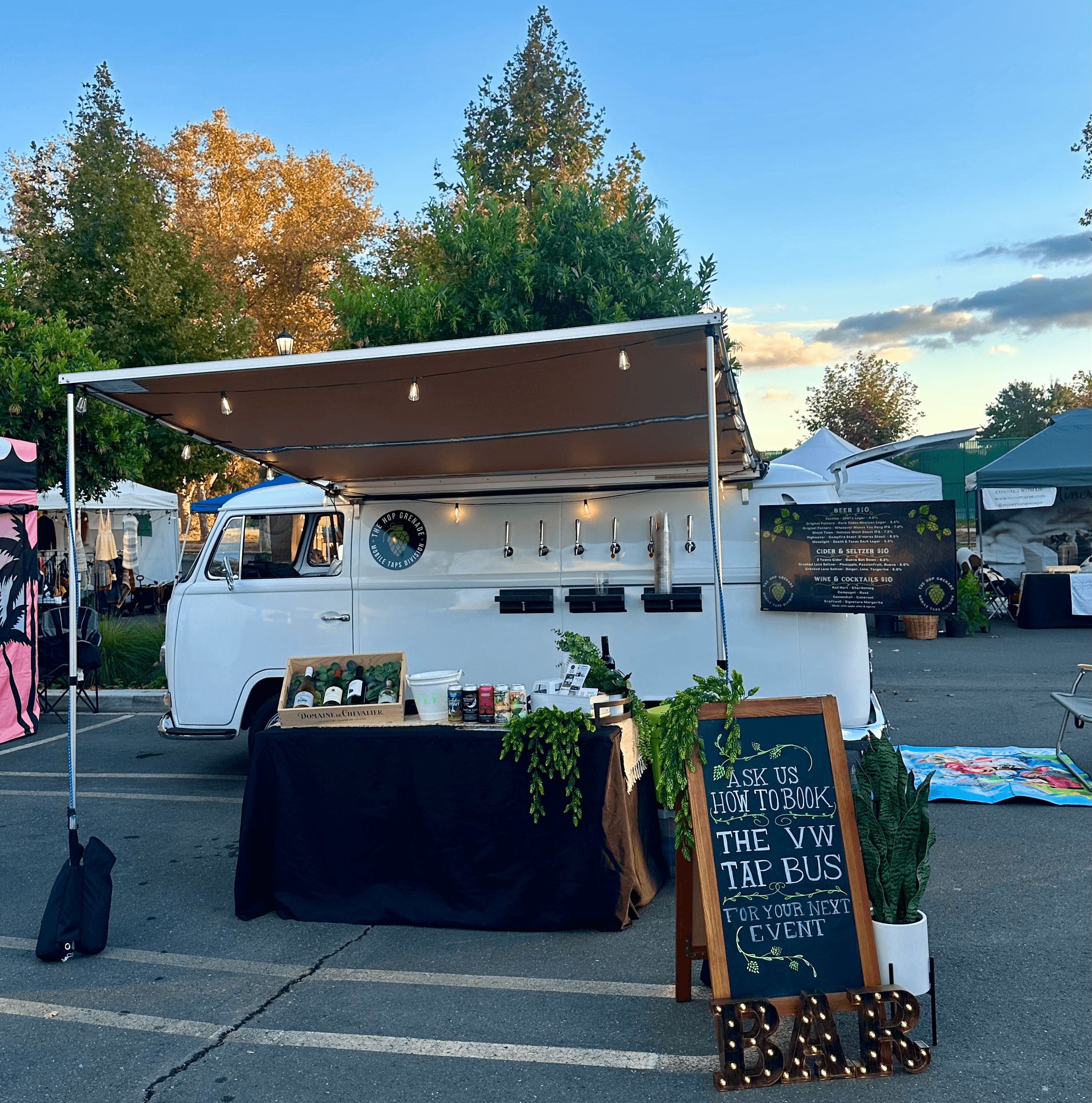White vintage VW bus mobile bar with beer taps, awning, and event signage outdoors.