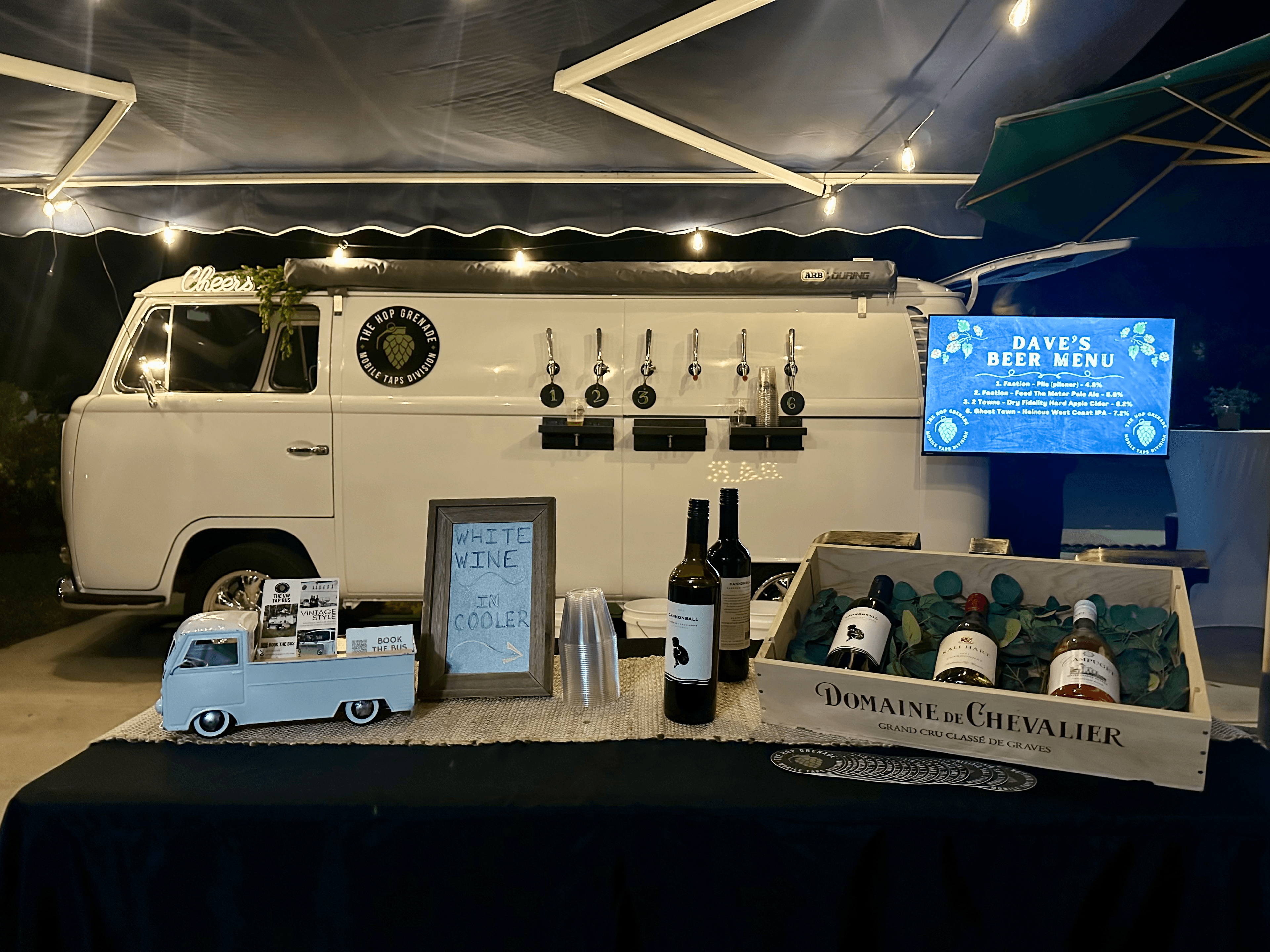 Vintage white VW bus mobile bar featuring beer taps and wine display under string lights.