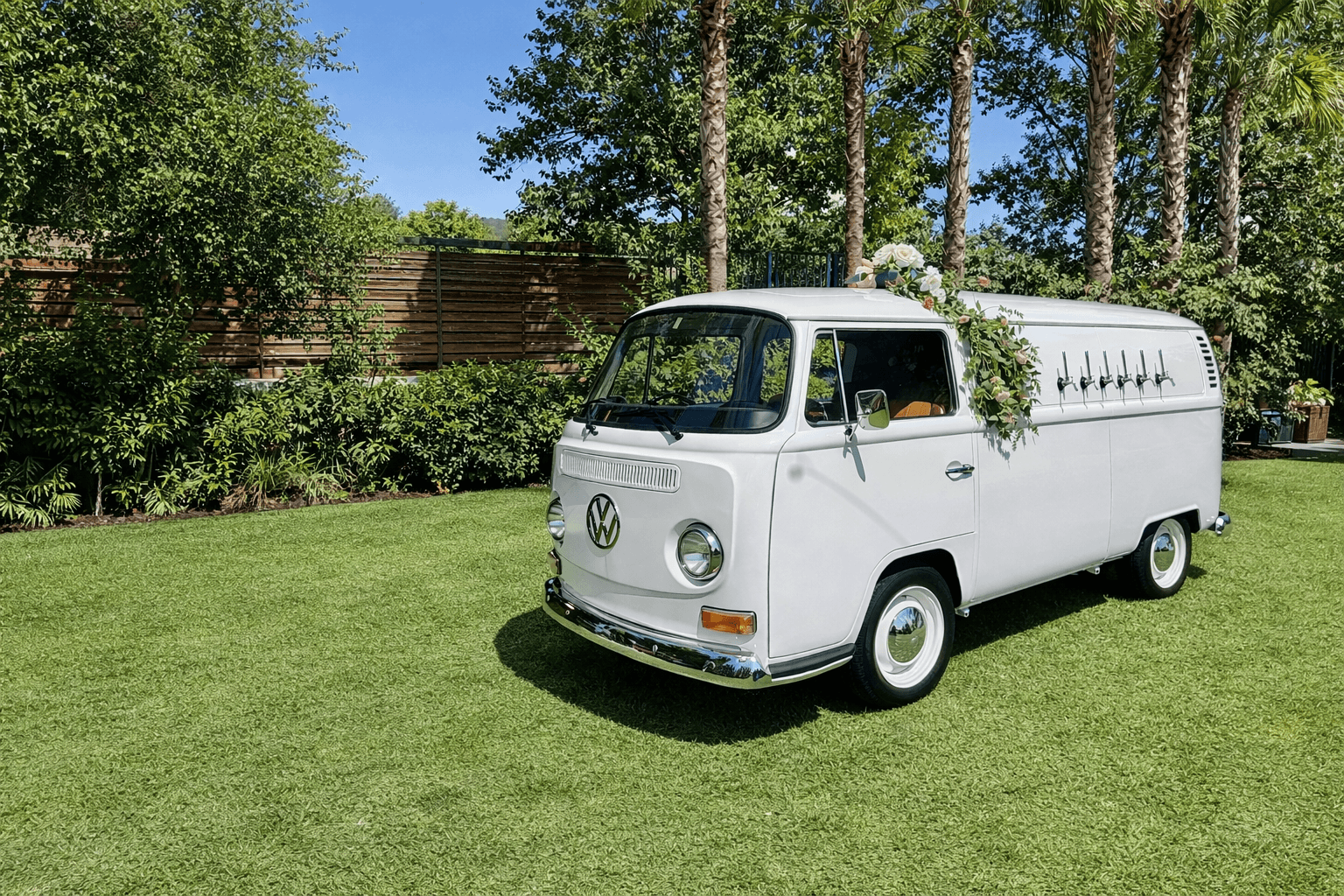 White vintage Volkswagen van mobile bar with beer taps and flowers on green grass.
